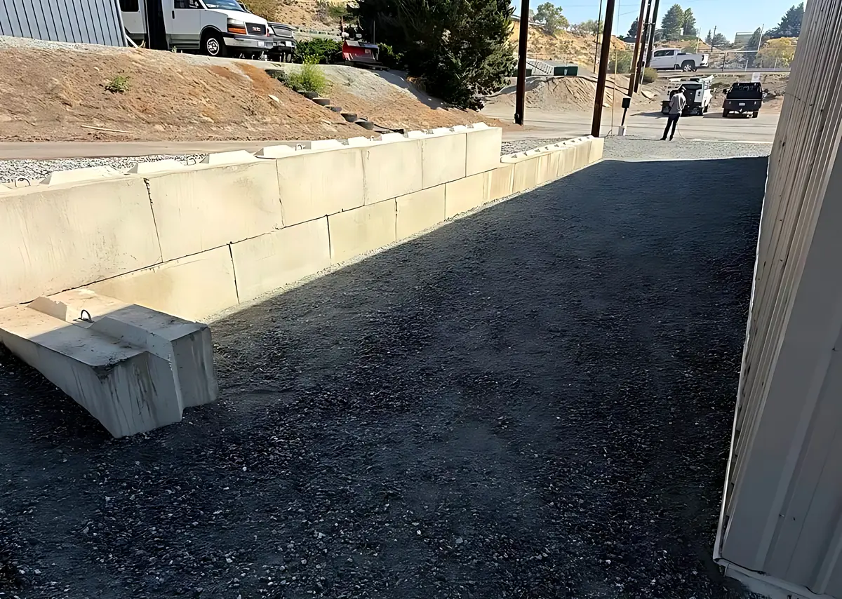 Large concrete block retaining wall beside a building with a new crushed rock surface along it