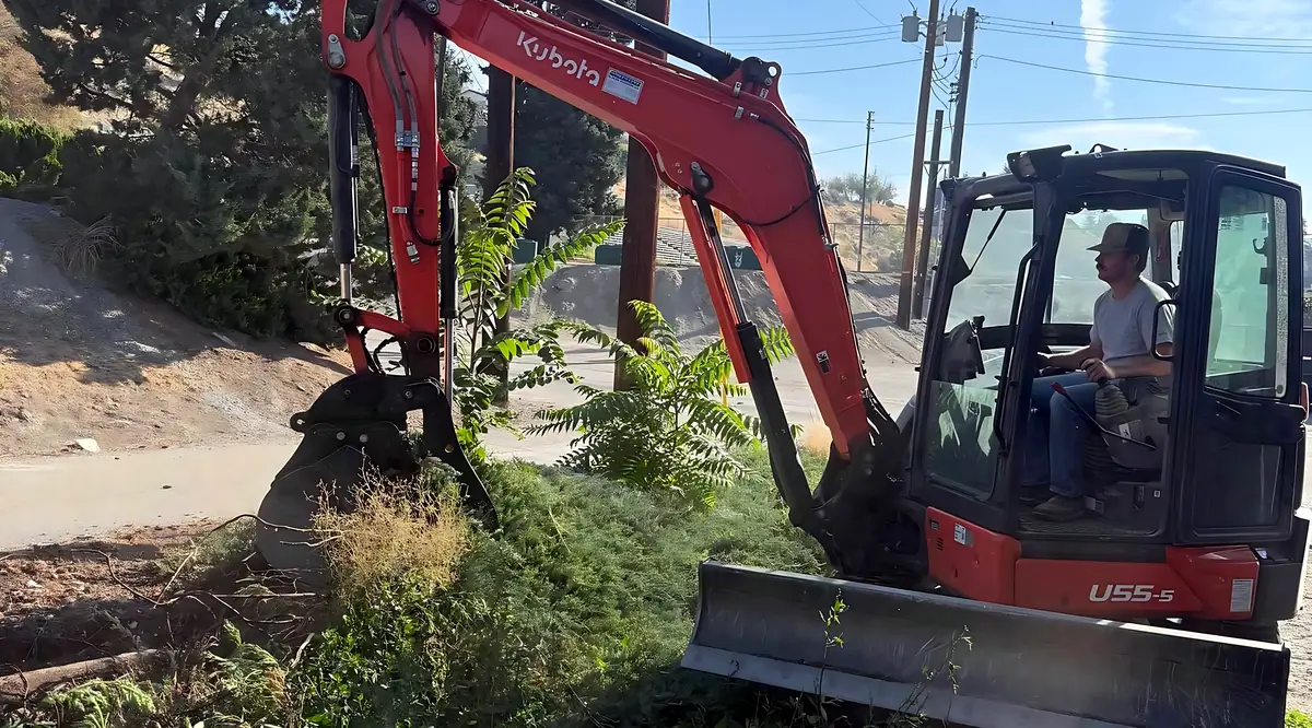 Kubota U55-5 excavator with an operator in the cab, clearing a roadside bank